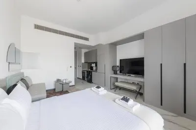 a white bedroom with a bed and a television at Brand New Studio 15 mins drive from Business Bay in Dubai