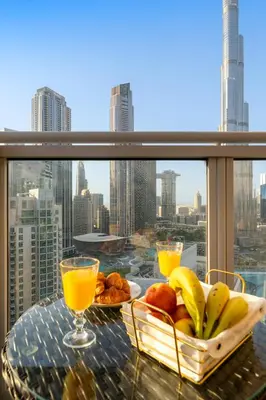 a table with a bowl of fruit and two glasses of orange juice at Ace Luxe, 2BR, Downtown, Burj Khalifa & Dubai Fountain view, 5 mins walk to Dubai Mall in Dubai
