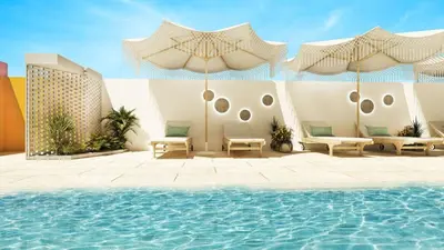 a pool with chairs and umbrellas next to a building at Cozy studio apartment in Jumeirah Village Circle in Dubai