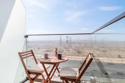 a table and chairs on a balcony with a view of the desert at Manzil - Stylish living in JVC, City Views and Pool in Dubai