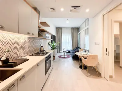a kitchen with white cabinets and a dining room at Cozy 1 Bedroom in Golfville Dubai Hills in Dubai