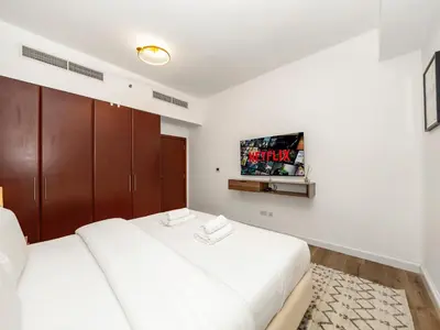 a white bedroom with two beds and a tv at Elegant Dubai Eye Beach Retreat in Dubai