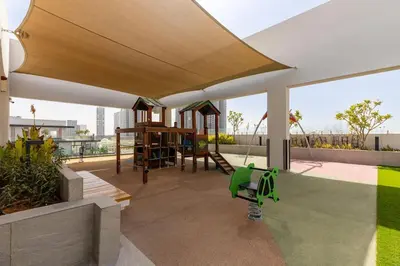 awning over a patio with a swing and a playground at Waves - Elegant Oxford 212 Studio in JVC with City Views in Dubai