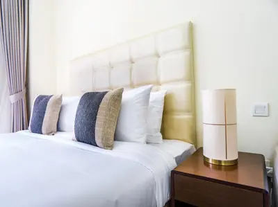 a white bed with pillows and a lamp on a table at EasyGo -Stylish STU With pool view Linkin park Arjan- 17 in Dubai