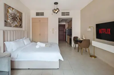 a hotel room with a white bed and a kitchen at Sunny Studio Perfect For Discovery Gardens Stays in Dubai