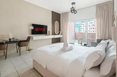 a hotel room with a large white bed and a table at Sunny Studio Perfect For Discovery Gardens Stays in Dubai