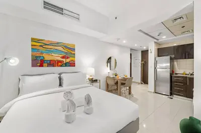 a bedroom with a large white bed and a kitchen at FIRST CLASS Studio Cozy Urban Retreat in Dubai