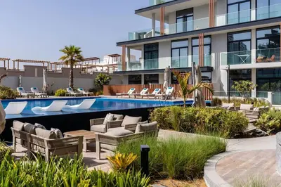 a resort with a swimming pool and chairs and a building at Waves - Comfortable JVC Apt with Balcony and Maids Room in Dubai