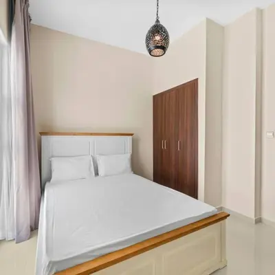 a bedroom with a white bed with a wooden cabinet at Modern 3-Bedroom Villa in Damac Hills 2 in ‘Ūd al Bayḑāʼ