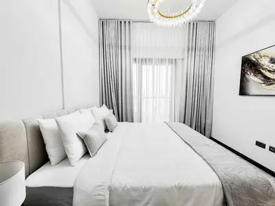 a white bedroom with a large bed and a chandelier at Upgraded 1BDR APT in Mag 930 , AL Merkadh Dubai in Dubai