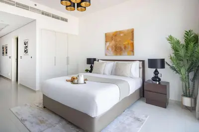 a white bedroom with a large bed and a table at Frank Porter - Damac Ghalia in Dubai
