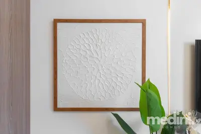 a picture in a frame on a white wall with a plant at 12min from Burj Khalifa - Studio - Azizi Riviera in Dubai