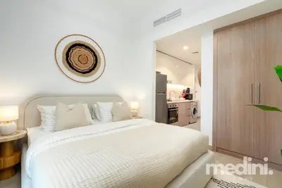 a bedroom with a large white bed and a kitchen at 12min from Burj Khalifa - Studio - Azizi Riviera in Dubai