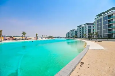 a large swimming pool next to a beach with buildings at 1BR Escape by the Lagoon in District One Meydan in Dubai