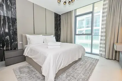 a bedroom with a white bed with a large window at Unique 1 Bedroom in District One Meydan in Dubai