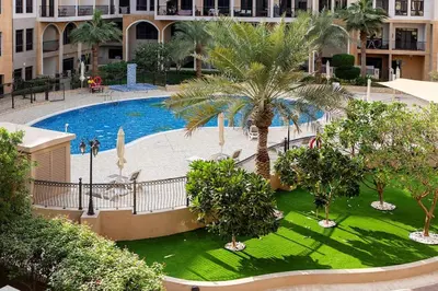 an outdoor pool with palm trees in a building at Bright 1Bdr at Fortunato in Dubai