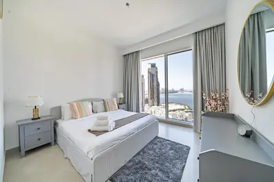 a bedroom with a large bed and a large window at Homes Beyond I 2 BR Apartment with Panoramic Creek View in Dubai