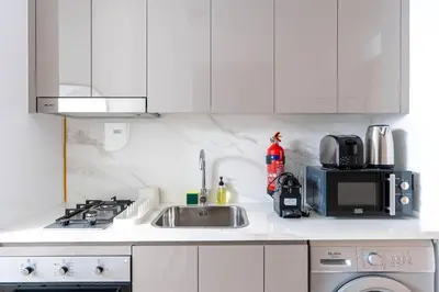 a white kitchen with a sink and a microwave at Nasma Luxury Stays - Trendy & Stylish Living Studio at Azizi Riviera 41 in Dubai