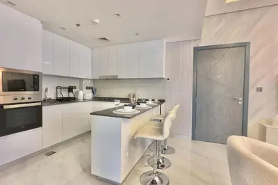 a kitchen with white cabinets and a bar with a stool at Relaxing 2BR Escape with Private Pool Samana GA by Vibel in Dubai
