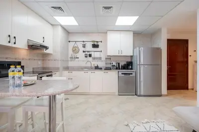 a kitchen with white cabinets and a stainless steel refrigerator at StayShort - Cozy 1-Bedroom Apartment for 5 in Motor City! in Dubai