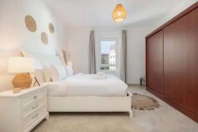 a white bedroom with a white bed and a dresser at StayShort - Cozy 1-Bedroom Apartment for 5 in Motor City! in Dubai