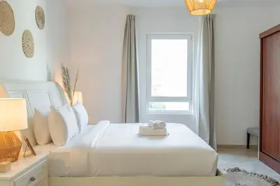 a white bedroom with a white bed and a window at StayShort - Cozy 1-Bedroom Apartment for 5 in Motor City! in Dubai