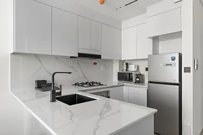 a white kitchen with a sink and a refrigerator at Vayk - Modern 2BR Apartment in Dubai