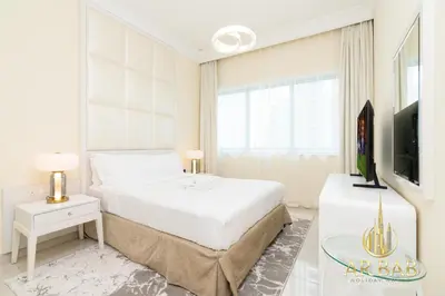 a white bedroom with a bed and a tv at Damac Maison Mall Street - Royal 3BR - Burj Khalifa View - Near Dubai Mall in Dubai