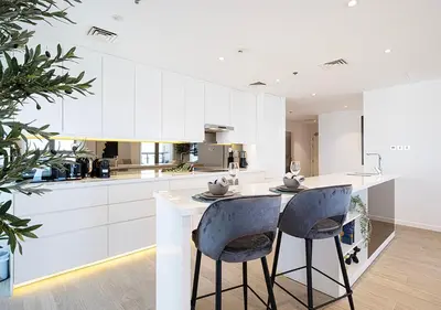 a kitchen with white cabinets and a island with two bar stools at Princess Tower - Spectacular Sky Views, Palm Jumeirah & JBR Beach in Dubai