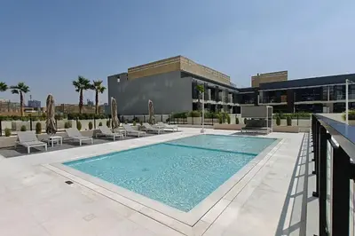 a swimming pool with chairs and a building at Vogue JVC Binghatti Corner near Circle Mall, One Bedroom Apartment with Balcony and City View, Access to all Amenities in Dubai