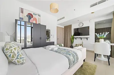 a white bedroom with a large bed and a living room at Modern Studio Near To Park in Dubai
