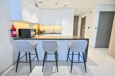 a kitchen with a counter and three bar stools at 1BR Close to Crystal Lagoon in District One Meydan in Dubai