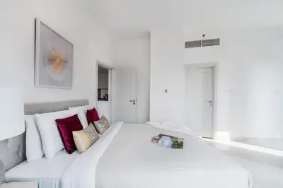 a white bedroom with a large white bed with red pillows at The Smart Concierge - Damac Heights in Dubai
