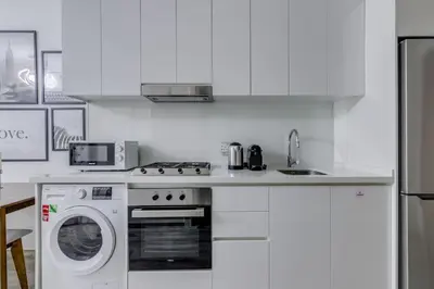 a white kitchen with a stove and a dishwasher at Knokey Ahad Residence in Dubai