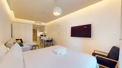 a bedroom with a white bed and a living room at Locations I Ahad Residences I Luxurious Studio Apartment I Business Bay I 10-Min Drive to Downtown Dubai & Burj Khalifa in Dubai