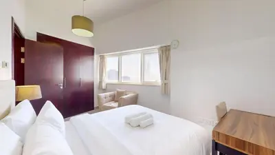 a bedroom with a bed with white sheets and a desk at The Bridge - Tranquil Two Bedroom in Sports City in Dubai