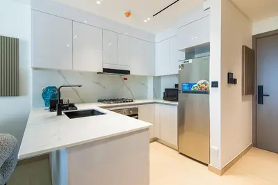 a kitchen with white cabinets and a stainless steel refrigerator at Binghatti Emerald, JVC- Charming 1-BR Apartment in Dubai