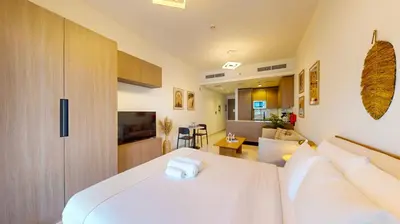a bedroom with a white bed and a living room at Avanos Residence - Captivating Studio in JVC in Dubai