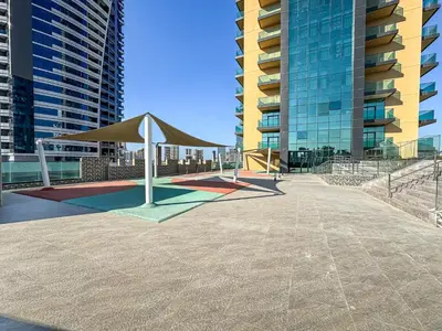 a playground with a tan umbrella in front of some buildings at Lovely Studio with Pool and Gym in Dubai