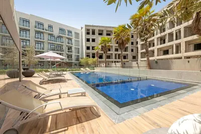 a large swimming pool with chairs and a building at Comfy JVC Studio Pantheon Comfort & Style by Vibel in Dubai
