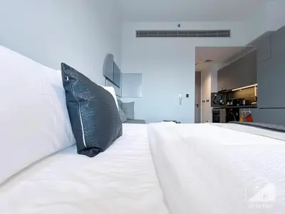 a large white bed with a black pillow on it at Modern Meydan Studio with Private Balcony in Dubai