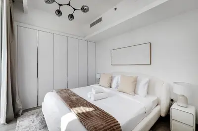 a white bedroom with a white bed and a chandelier at Bright 1BR with balcony in Luma 22 in Dubai
