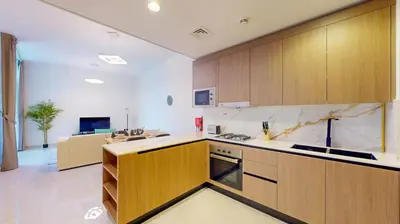 a large kitchen with wooden cabinets and a living room at Locations I Avanos Residence I Premium Modern 1BR I Cosy & Comfortable I Near Parks, Shops & Cafés in JVC in Dubai