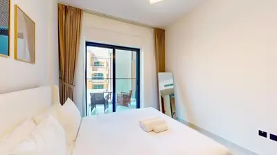 a bedroom with a white bed and a balcony at Locations I Avanos Residence I Premium Modern 1BR I Cosy & Comfortable I Near Parks, Shops & Cafés in JVC in Dubai