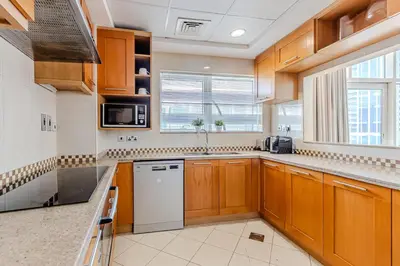 a kitchen with wooden cabinets and a white dishwasher at Spacious 3BDR Apartment in Marina with Office in Dubai