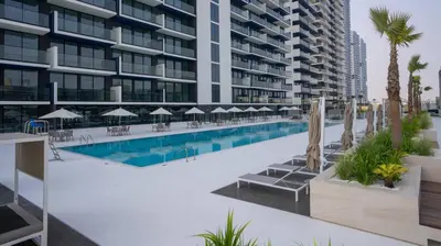 a swimming pool with chairs and umbrellas next to a building at Modern 1br In Jvc Pool, Balcony & Free Parking in Dubai