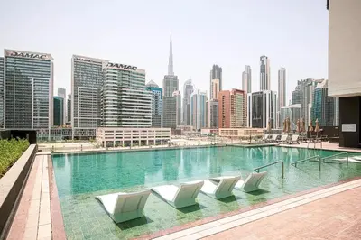 a swimming pool with white chairs and a city skyline at 2BR with Extra-Large Balcony Canal & Burj Views by Vibel in Dubai