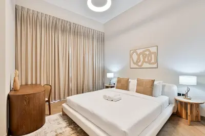 a white bedroom with a large bed and a table at Modern 2 BR Apartment near Dubai Butterfly Garden in Dubai