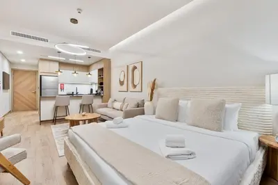 a white bedroom with a large bed and a living room at Modern Studio with Pool, Gym and BBQ area in Dubai