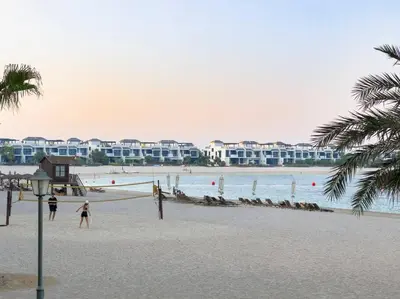 two people walking on a beach with buildings in the background at FIRST CLASS 2BR Cozy Beachfront Escape in Dubai